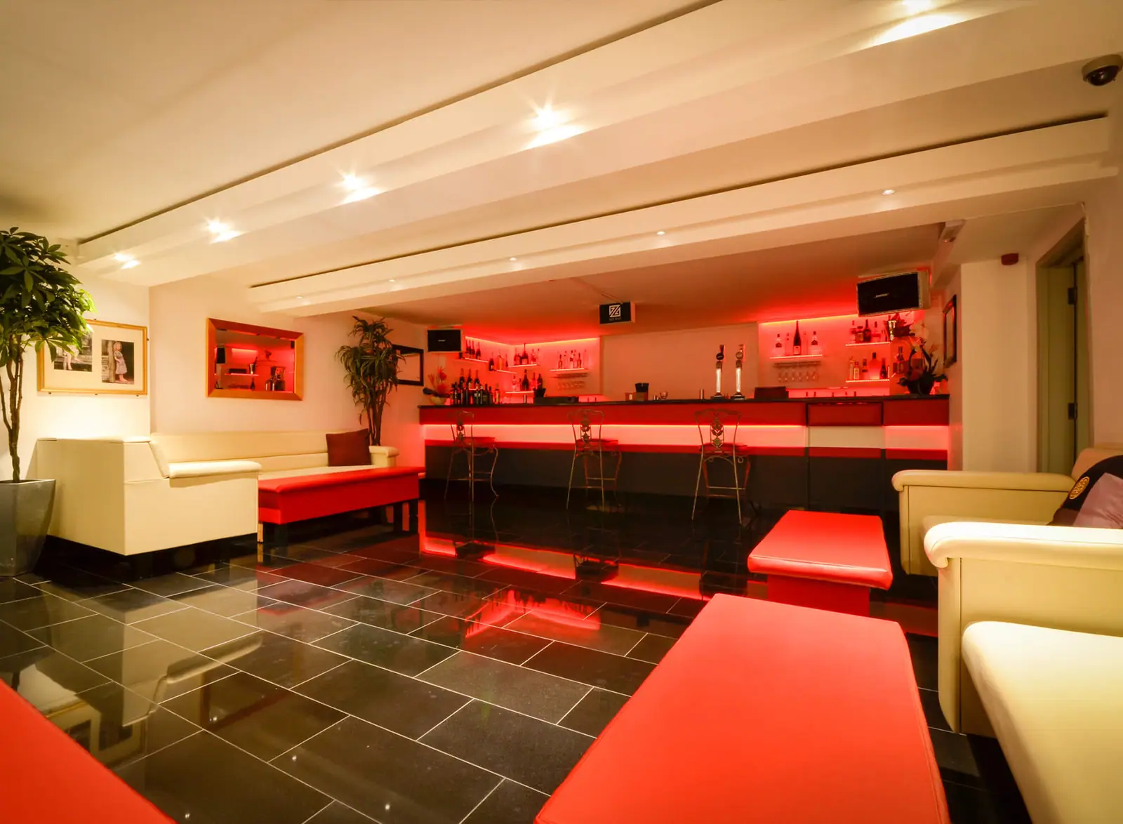 Basement nightclub lounge with red seating and a backlit bar