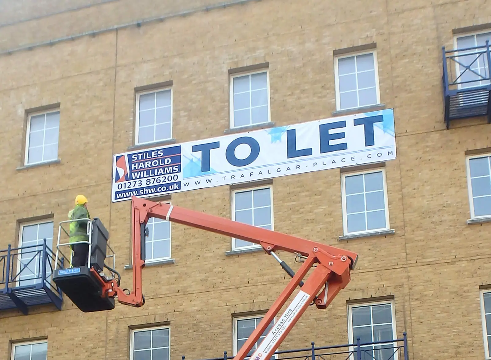 Installer fitting the high-level 'to let' banner from a cherry picker